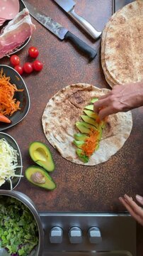 overhead view cropped female hands preparing food, making sandwich wrap with soft flatbread and healthy ingredients