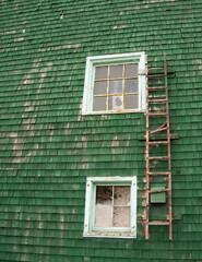 two windows and one ladder on a green wooden shingled home exterior wall in need of repair with peeling paint grunge vintage style look vertical image with room for type home window repair background 