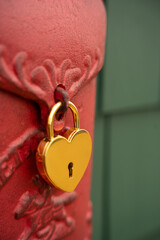 gold heart shaped lock locked onto red metal door with green wooden shingles in background empty space for type symbol for love valentines romance heart health and security 