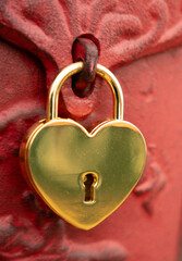 shiny gold heart shaped lock hanging from clasp on  red metal background vertical photo with room for type love heart cherish romance valentines connection background or backdrop
