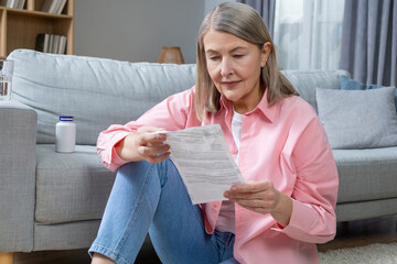 Mid aged woman in pink shirt reading description to medicine and looking concentrated