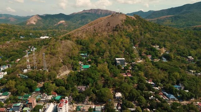 Mount Tapyas hillside landmark rises above Coron town in Palawan with telecom towers winding paths hillside homes and green mountain ridges under a partly cloudy sky