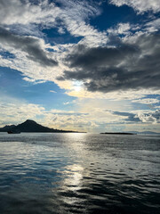 A serene seascape at golden hour featuring dramatic clouds, calm ocean waves, and distant mountains. Perfect for travel promotions, meditation themes, or nature-inspired wall art that evokes peace