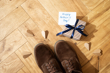 Father day greeting card. Gift box, paper hearts and man shoes on the wooden oak parquet flooring background.