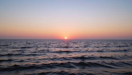 Obraz premium Sunset over calm ocean waters with gentle waves.