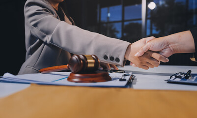 Two businesspeople are shaking hands in a law office with a scale and a gavel on the table.