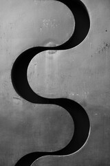 wavy metal cut out of a silver chrome metal wall s shaped shadow in separation of two sides flowing...