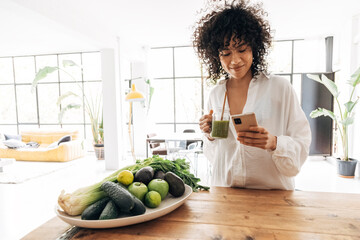 Young african american woman looking at her phone, browsing through social media while having a...
