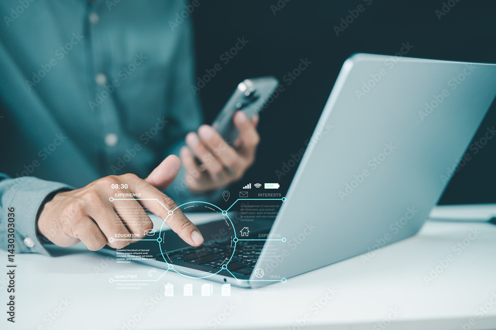 Poster a person uses a laptop while holding a smartphone, with digital interface elements displayed, sugges
