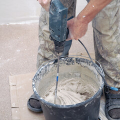 A worker stirs the construction mixture plaster in a bucket with an electric stirrer. Repair in the apartment with your own hands