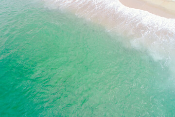 aerial view of turquoise water meeting sandy beach, drone shot of waves and foam on a clear beach