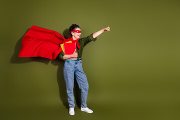 Confident mature woman with grey hair wearing a superhero red cape and holding notebooks on a green background © deagreez