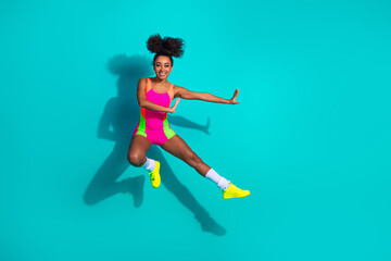Fototapeta premium Energetic young woman jumping in vibrant activewear against a teal background, embodying fitness, joy