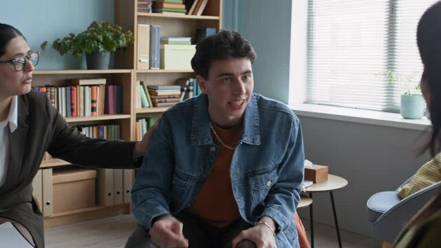 Slowmo zoom in shot of Caucasian teen boy getting angry and yelling at girl during therapy consultation with young biracial female psychologist trying to de-escalate high-conflict situation