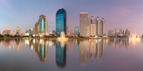 Panoramic view of Benjakitti Park with water fountains and city skyline in Bangkok, Thailand at dusk