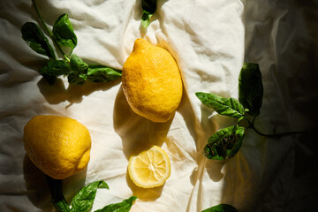 A collection of fresh lemons and vibrant basil leaves is artistically arranged on a light fabric...
