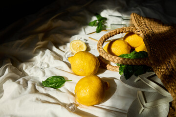 Lemons rest in a woven bag alongside fresh mint leaves and glassware, creating a vibrant summer...