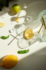 Bright sunlight casts playful shadows on lemon slices and basil leaves on a white surface