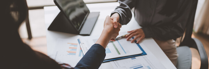 Business partners shaking hands after agreeing on a project, closing a deal or signing a contract, with documents and a tablet on a white table