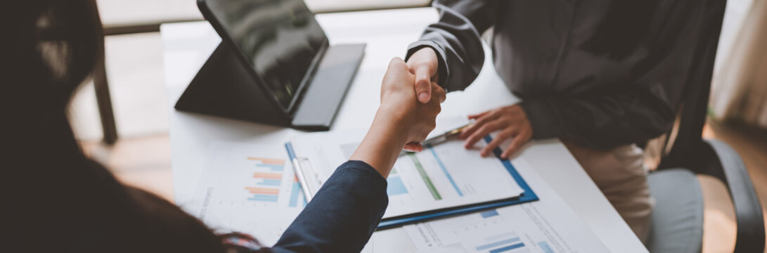 Business partners shaking hands after agreeing on a project, closing a deal or signing a contract, with documents and a tablet on a white table