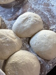 Several dough balls rest close together on a floured wooden surface, their soft, smooth texture and round shapes ready for baking.