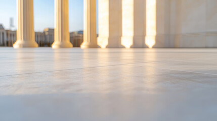 Fototapeta premium A low angle perspective shows sunlit marble columns in a row leading towards a blurred cityscape under a blue sky on a clear day creating architectural beauty.