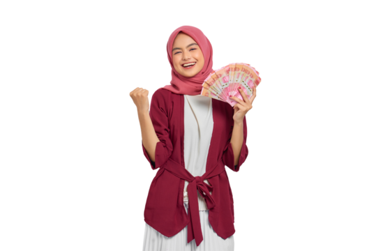 Excited young Asian Muslim woman in hijab holding Indonesian rupiah banknotes and celebrating financial success isolated on transparent background