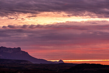 Sunset over vineyard rows and mountains in La Rioja, Spain, with dramatic sky and vibrant colors, evoking calm, nature, and seasonal agricultural cycles for stock imagery.