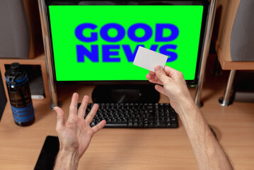 Excited young man with credit card looking at computer screen with message good news. Man at computer, keyboard visible, reacting positively to news on chromakey screen