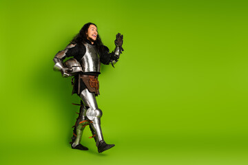 Young man dressed as a medieval knight in full armor with a vibrant green background