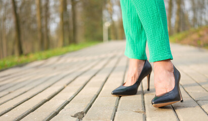 female legs in black stiletto heels on a path in the park