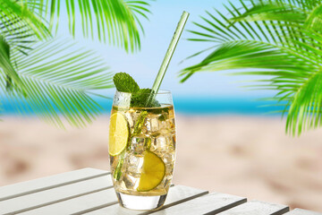 Refreshing cocktail on wooden deck under green palm leaves on tropical beach