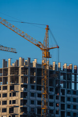 Fototapeta premium Tower cranes are working on the construction site of a new residential building, lifting heavy materials against a backdrop of a clear blue sky