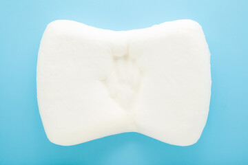 Hand imprint on clean white orthopedic memory foam pillow on light blue table background. Pastel color. Checking hardness and softness. Closeup. Top down view.