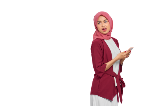 Annoyed young Asian Muslim woman in hijab holding smartphone while looking away with displeased expression isolated on transparent background