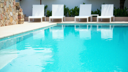Naklejka premium Blue swimming pool water and white poolside chairs