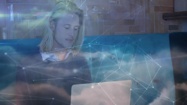 IT pro leaning on teal sofa, interacting with laptop overlaying cloud network graphics