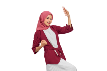 Excited young Asian Muslim woman in hijab celebrating success with smartphone and showing victory gesture isolated on transparent background