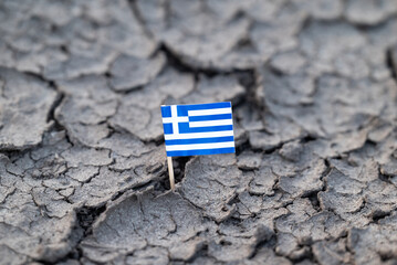 Greek flag stuck in cracked dry earth. Small flag of Greece placed in dry, cracked soil,...