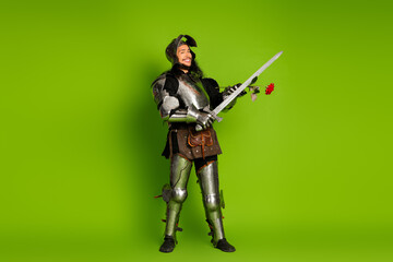 Young man dressed as a medieval knight holding sword and rose on a vibrant green backdrop