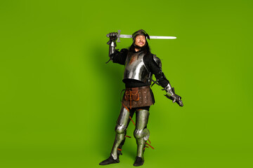 Male dressed as a medieval knight with sword in a metallic costume on vibrant green background