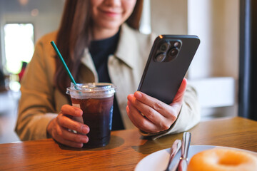 Closeup of a woman holding and using mobile phone while drinking iced coffee and eating donut at...