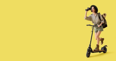 Surprised young traveler with binoculars riding electric kick scooter on yellow background with space for text © Pixel-Shot