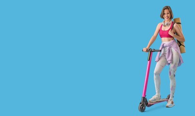 Sporty young woman with yoga mat and kick scooter on blue background with space for text