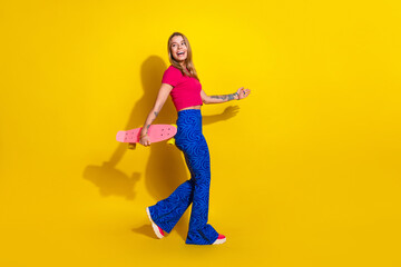 Stylish young woman with a pink skateboard against a vibrant yellow background expressing joy and...