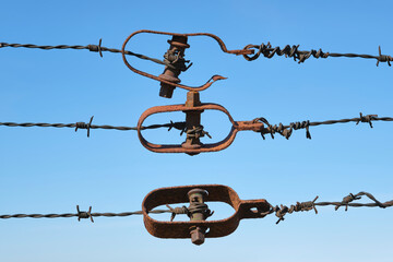 Closeup of three rows of old rusty and weathered barbed wire with tensioners against a deep blue sky