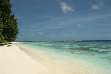 Sunny tropical beach with pristine white sand and clear turquoise water in the Maldives 