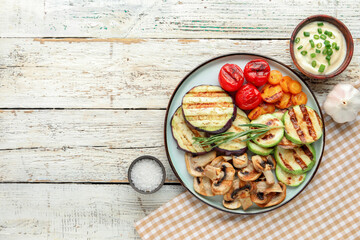 Plate with grilled vegetables and sour cream on white wooden background
