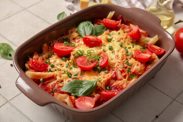 Baking dish of pasta with tomato sauce and cheese on white tile background