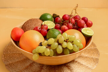 Bowl with different fresh fruits on orange background